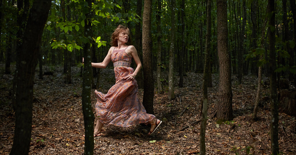 a girl in a pink dress being chased in a forest