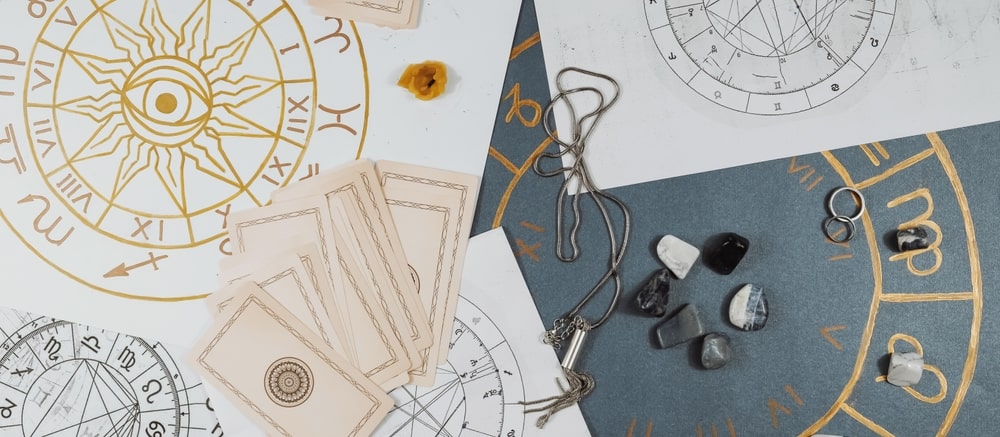 Birth charts and natal charts are spread out on a table along with astrology stones and planetary cards.