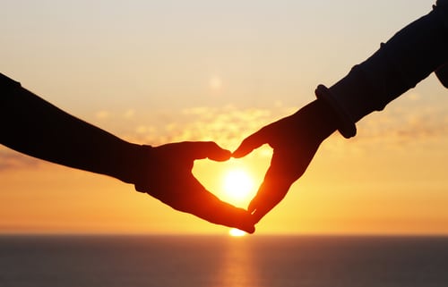 A close-up of a couple’s hands forming a heart at sunset
