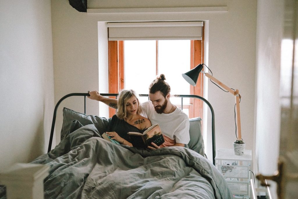 man and woman reading book on bed