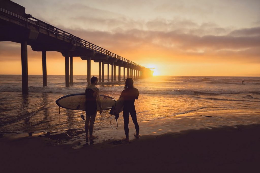 woman carrying surfboard beside person during sunset