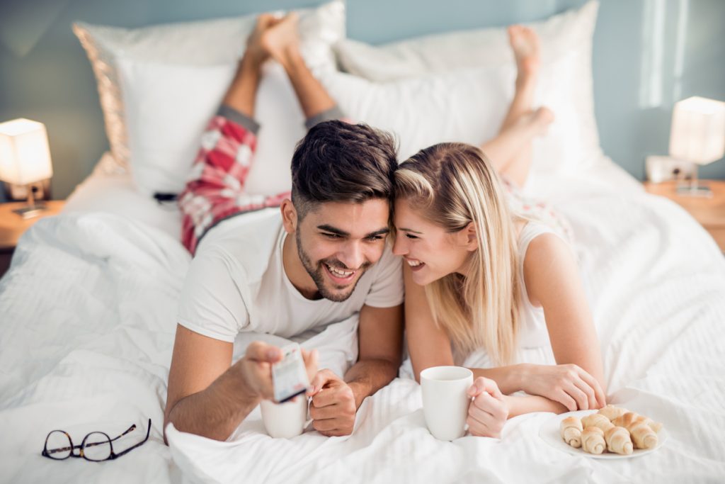 Young couple waking up and watching TV