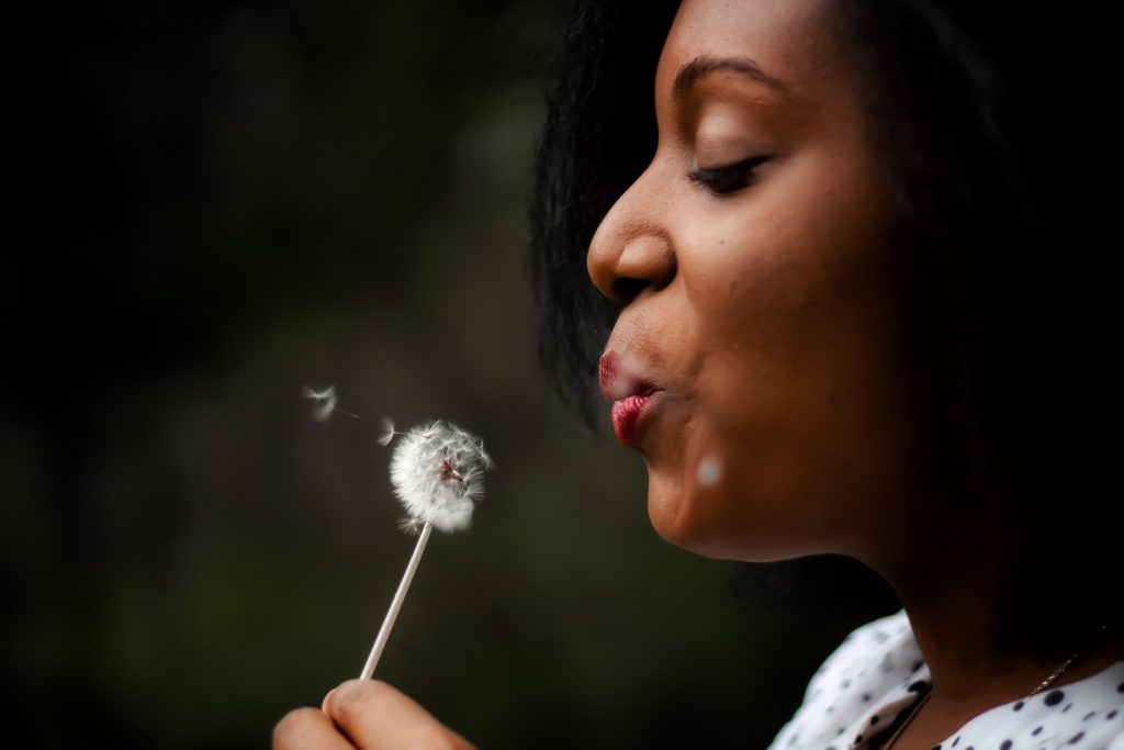 woman wistfully blowing a dandelion