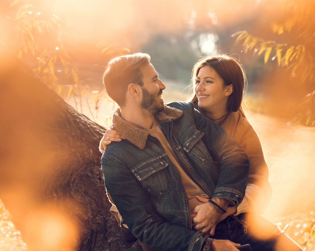 happy couple sitting against autumn tree