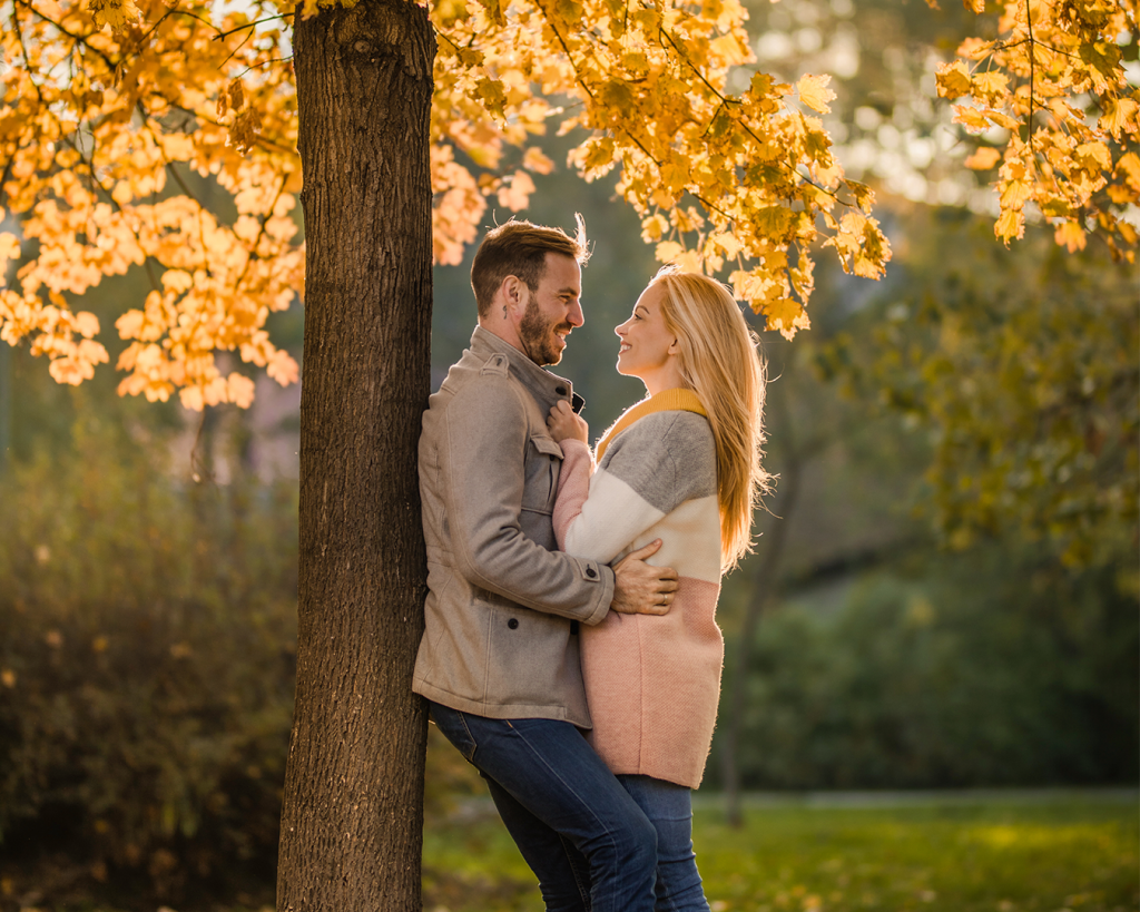 couple leaning against tree under fall leaves