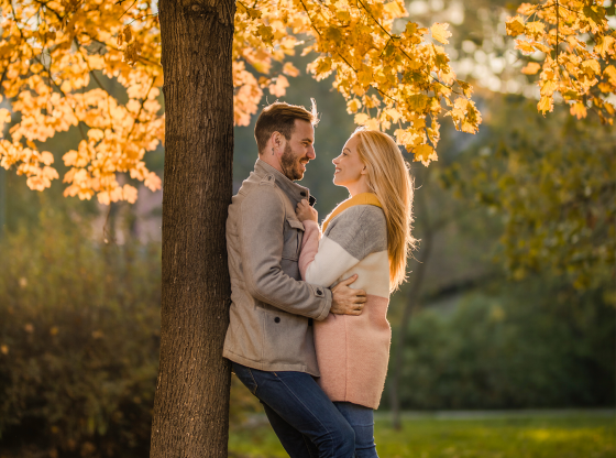 couple leaning against tree under fall leaves