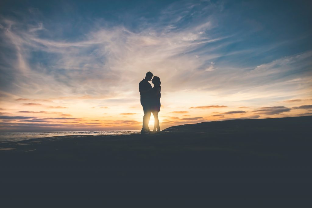 Silhouette of two people standing closely in front of the setting sun
