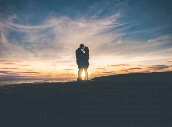 Silhouette of two people standing closely in front of the setting sun