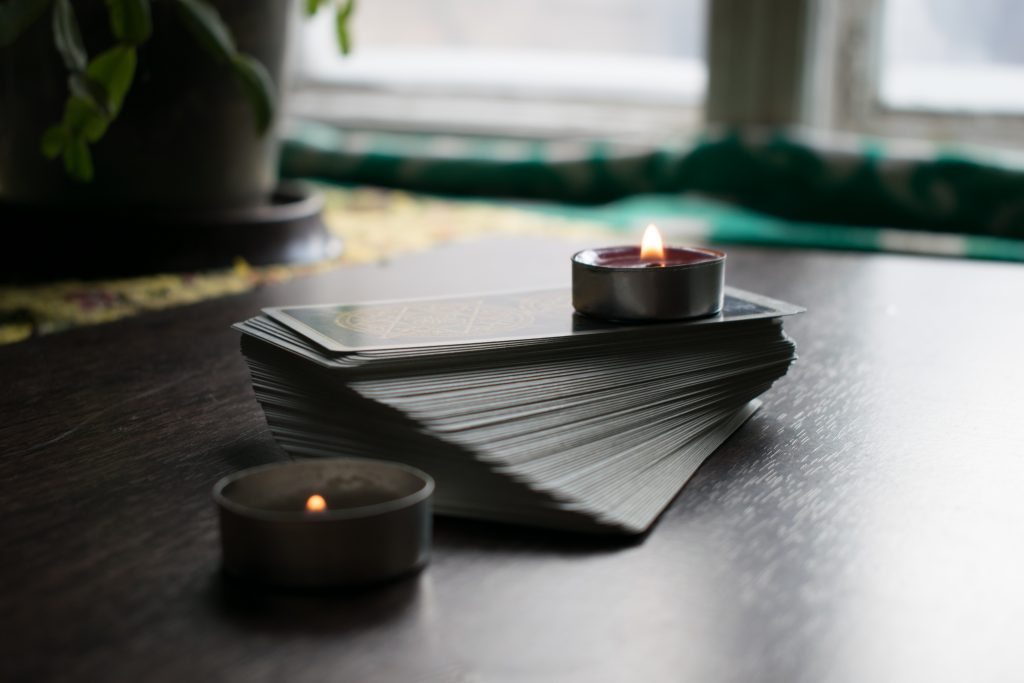 A splayed deck of cards on a table, surrounded by candles.