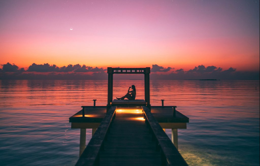 silhouette of person sitting by the water at sunset