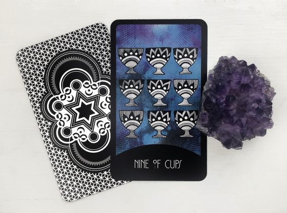 Nine of Cups Reversed Tarot Card illustration showing a figure sitting alone at a table with nine cups, some overturned, symbolizing unmet expectations and emotional imbalance.