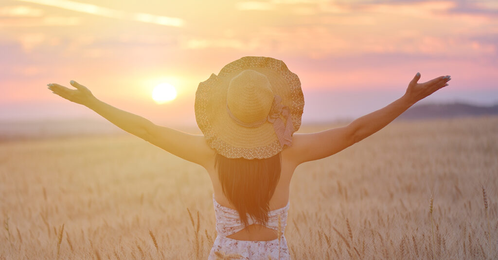 a woman standing in the middle of a prairie feeling free and looking at the sunset