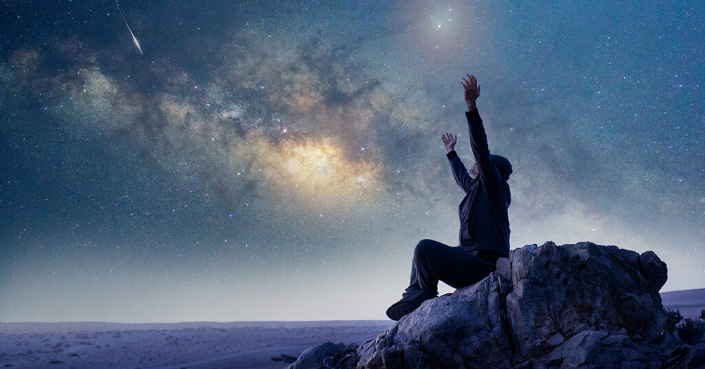a person sitting on a rock under the stars with their arms spread wide open
