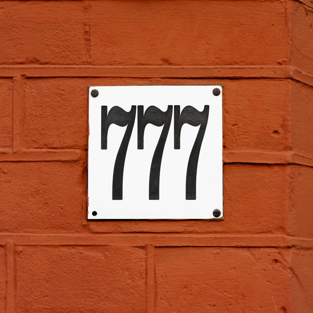 The address number 777 on a red brick wall.