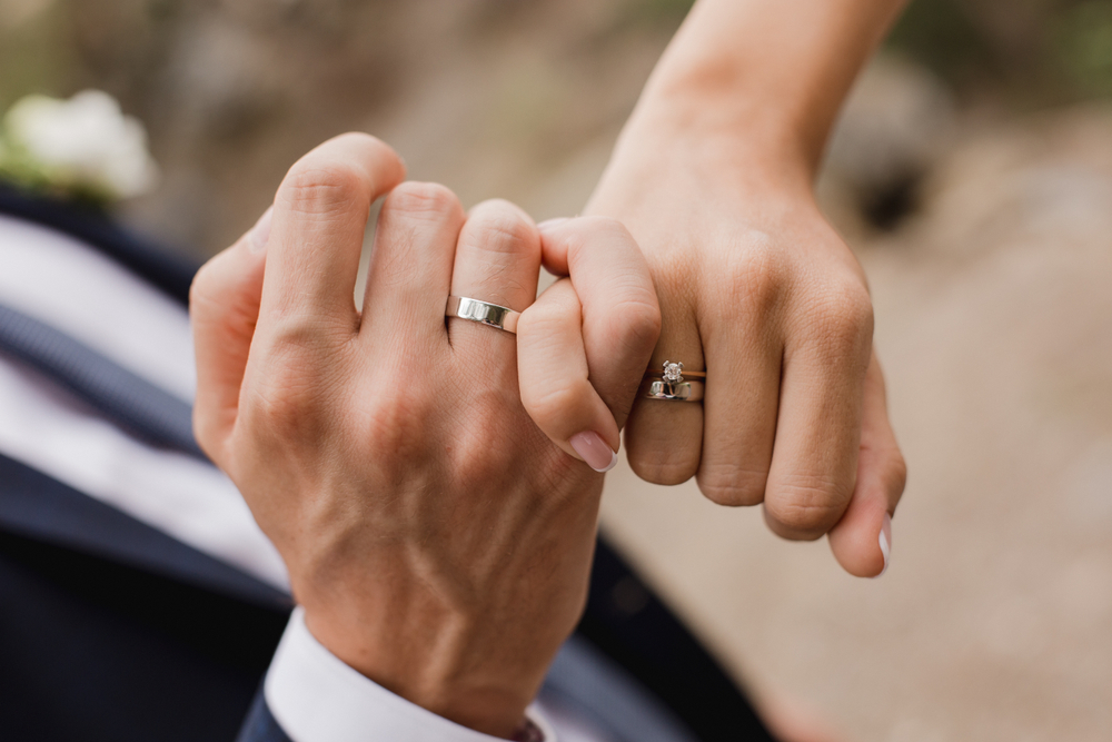 Man and woman intertwining pinky fingers with wedding rings on their hands.