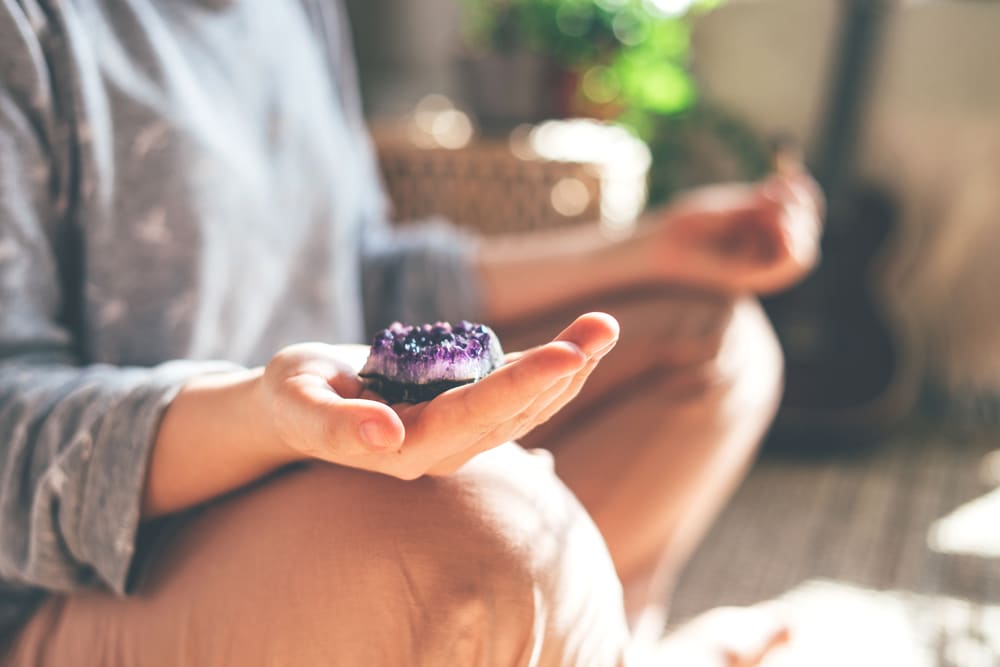 A woman is meditating with a crystal quartz in her hand. She sits on the floor at home.