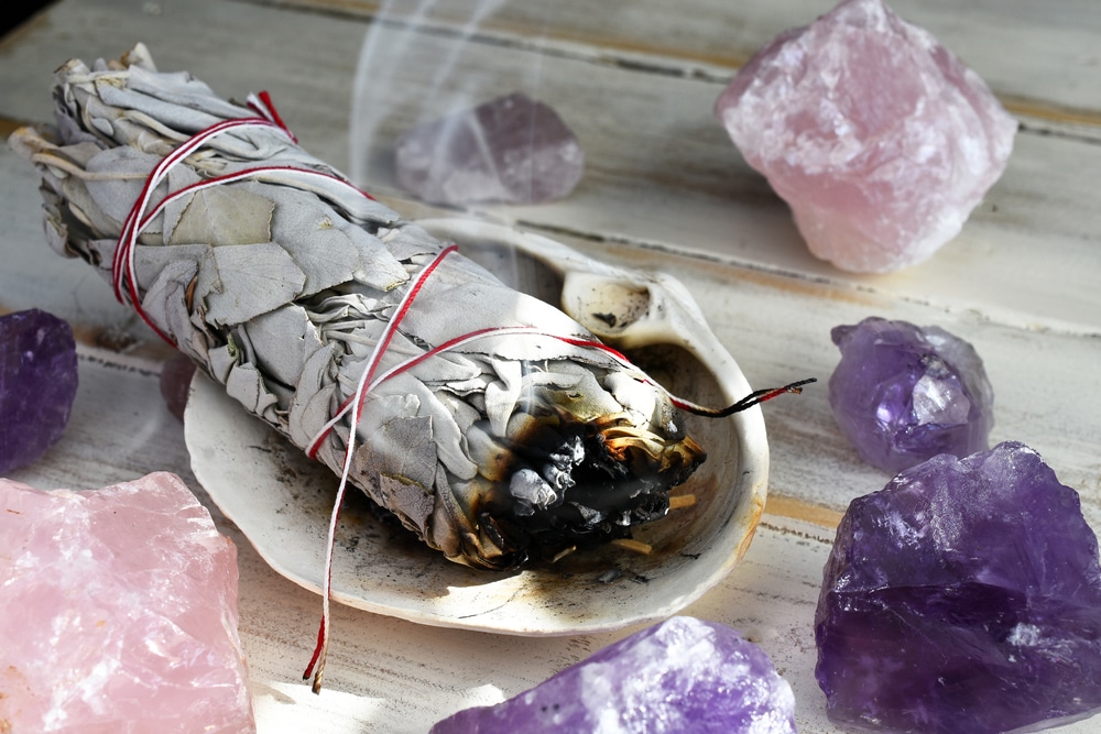 A close up image of a burning white sage smudge stick in a house used for energy clearing and healing