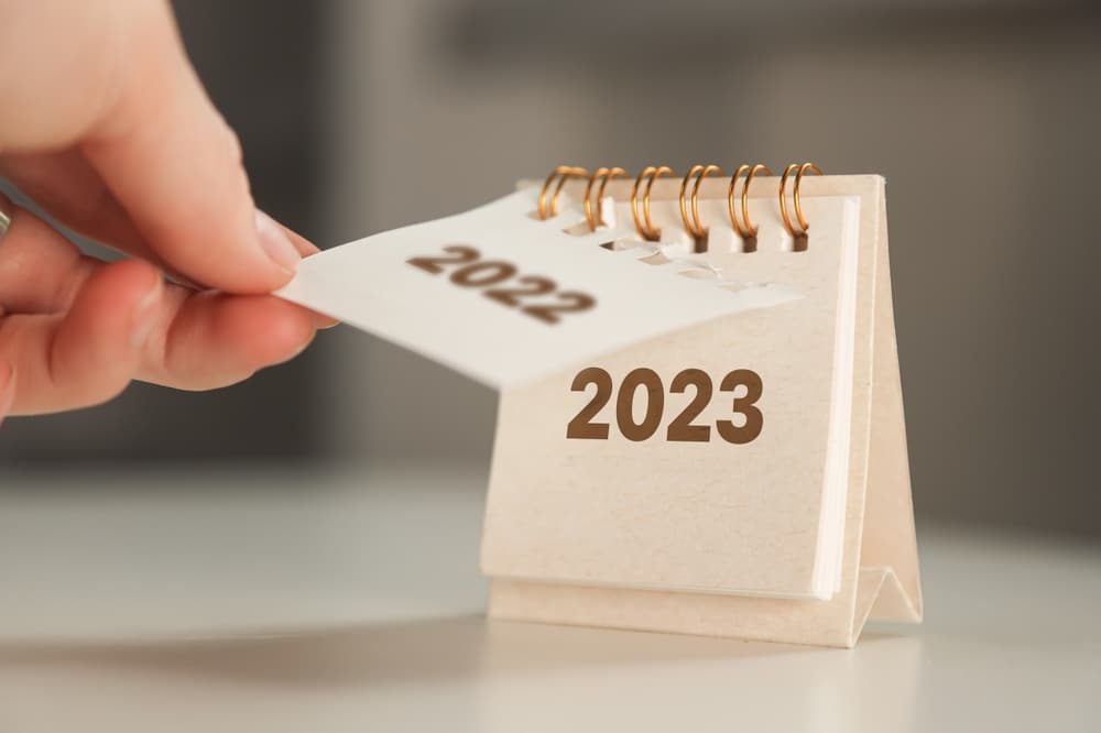 A woman's hand turns over a calendar sheet. The year changes from 2022 to 2023.