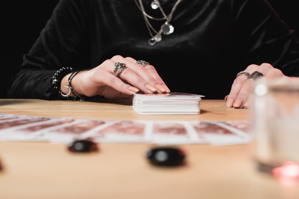 A psychic sits at a table and lays out oracle cards near divination stones during a psychic reading.