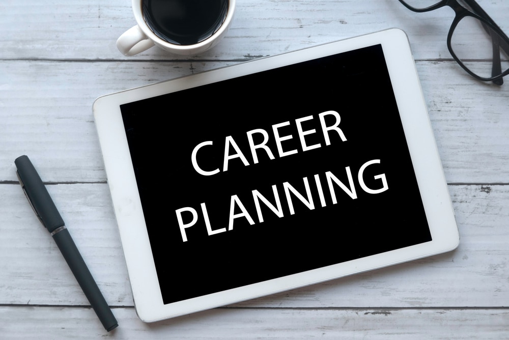 Top view of a cup of coffee, pen, glasses and tablet written with Career Planning on white wooden background.