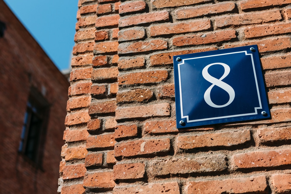 Alt Tag(s): Life path number 8 nameplate that states "Number 8" on a red brick wall.
