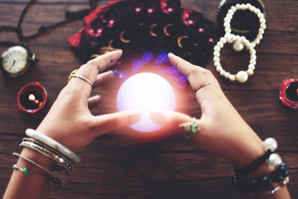 Close-up of a cheap psychic’s hands hovering over a crystal ball.