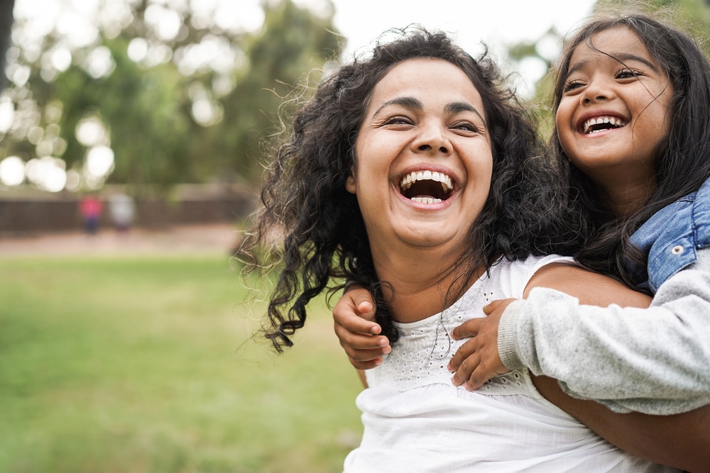 A woman giving her young daughter a piggyback ride and laughing.