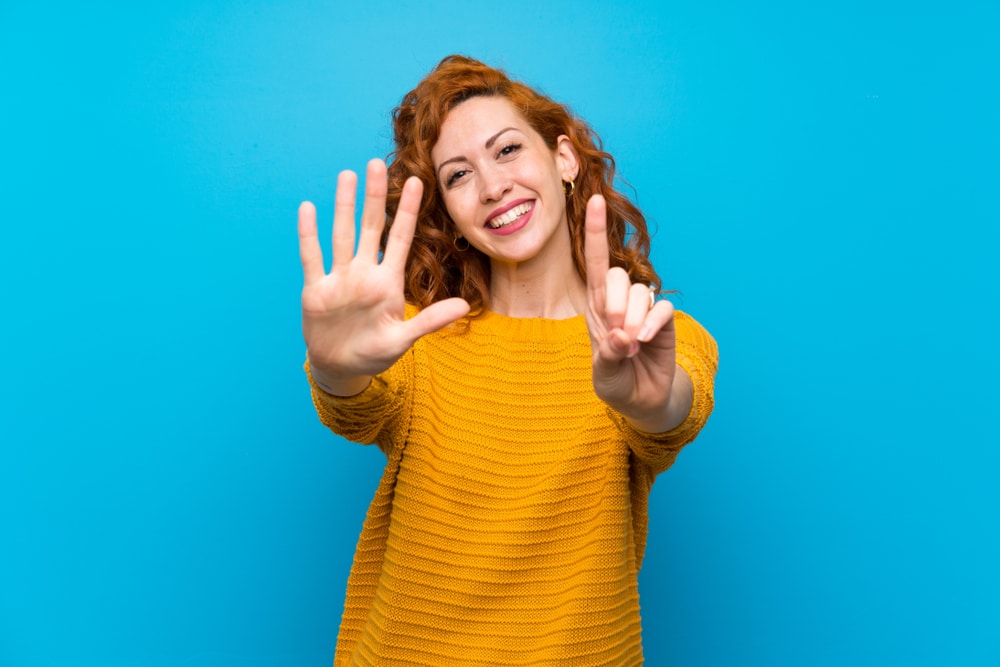 Redhead woman in a yellow sweater holding up 6 fingers