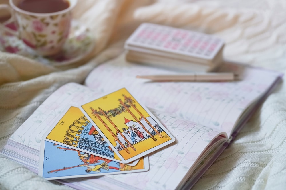 Close up of tarot cards, journal, pen, and coffee cup on a table.