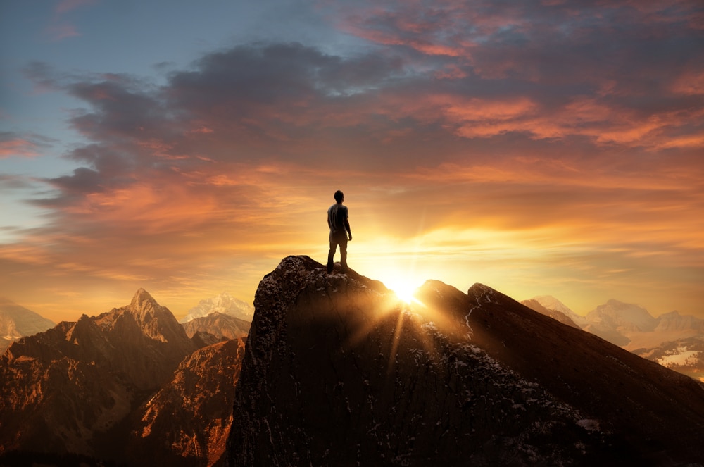 A man standing on top of a mountain as the sun sets.
