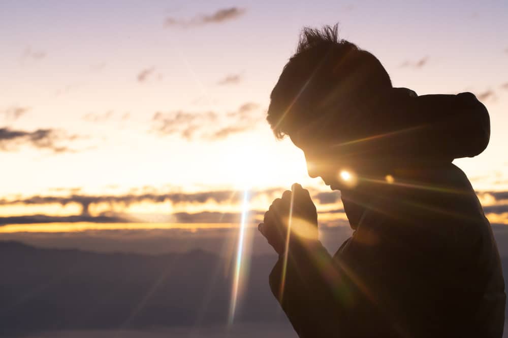 Silhouette of a man praying outside at sunset.