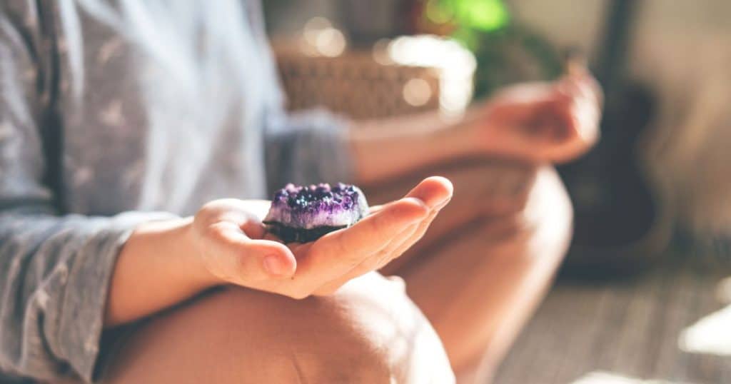 Person holding amethyst stone while meditating on the floor