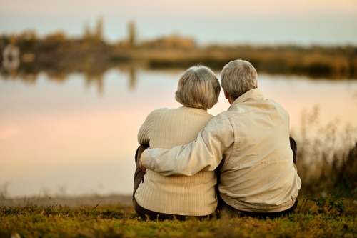 A senior couple cuddling and looking at a lake.